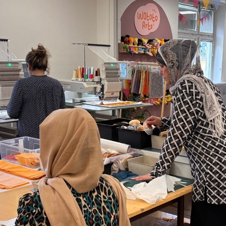 Three women with their backs turned, working on the production of dolls.