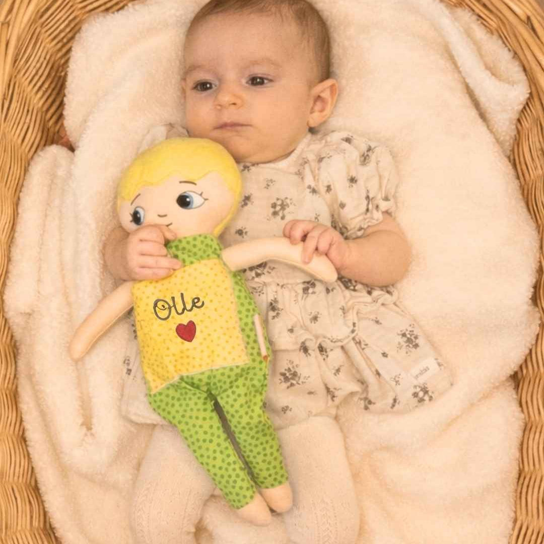 Dockan Adam som blir kramad av ett spädbarn som ligger i ett babynest