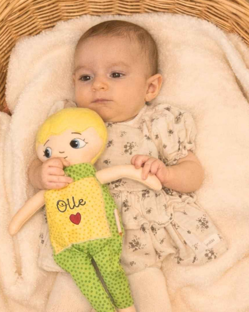 Dockan Adam som blir kramad av ett spädbarn som ligger i ett babynest