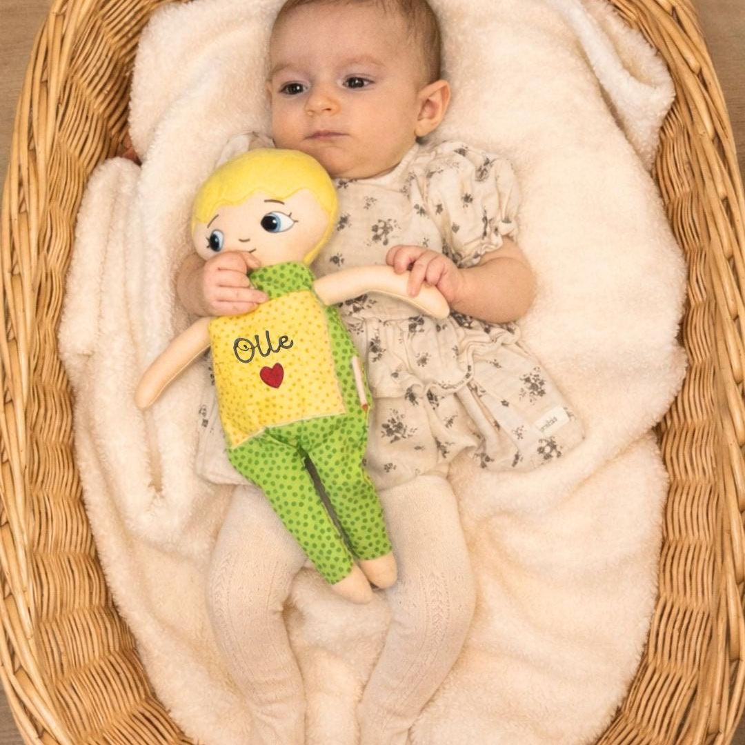 bebis ligger i korg och håller mjuk docka i gröna kläder