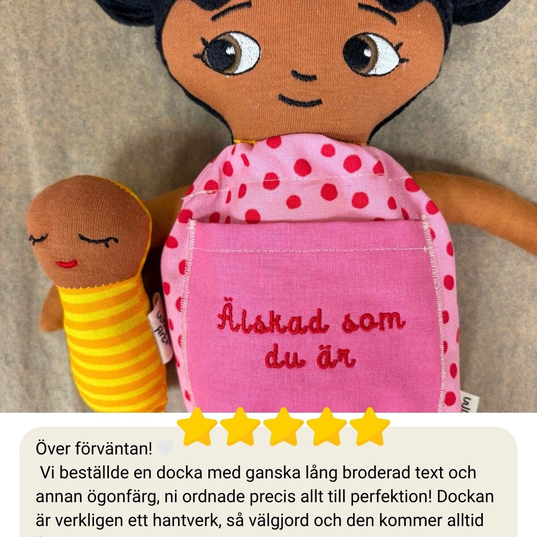 närbild på mjuk docka med personlig brodyr på klänning och en bebisdocka bredvid