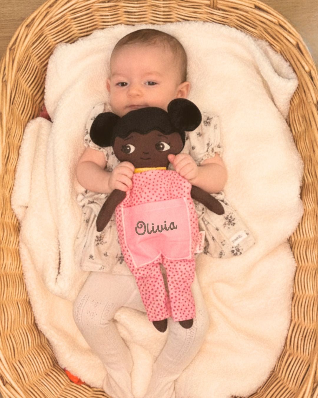 en bebis i en flätad korg och kramar dockan Amari