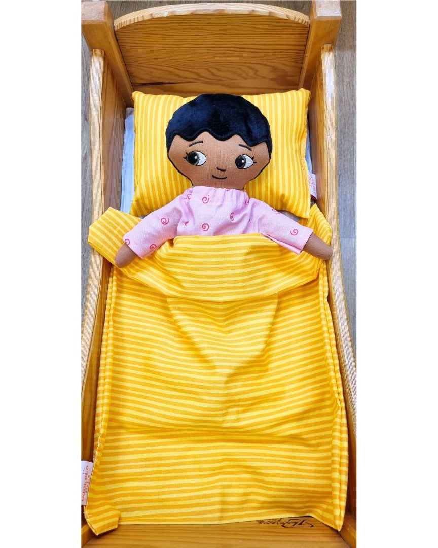 Pojkdocka från Watoto arts som bär pyjamas och liggen under det orangea täcket.