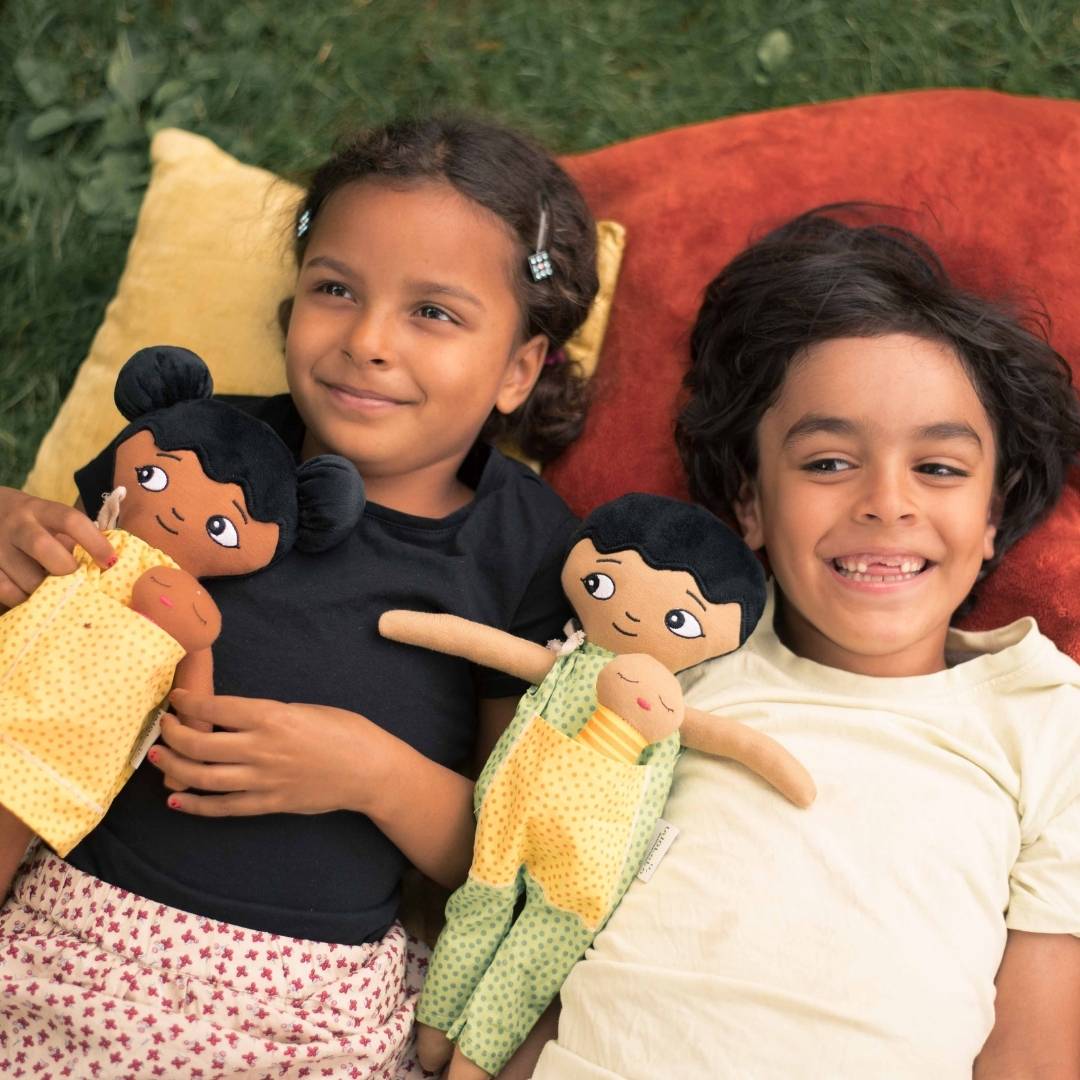 Två barn som leker med watoto arts normbrytande dockor, dockorna speglar barnens utseende.