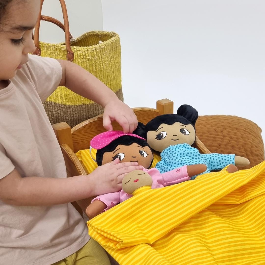 Flicka som leker med två dockor i docksäng