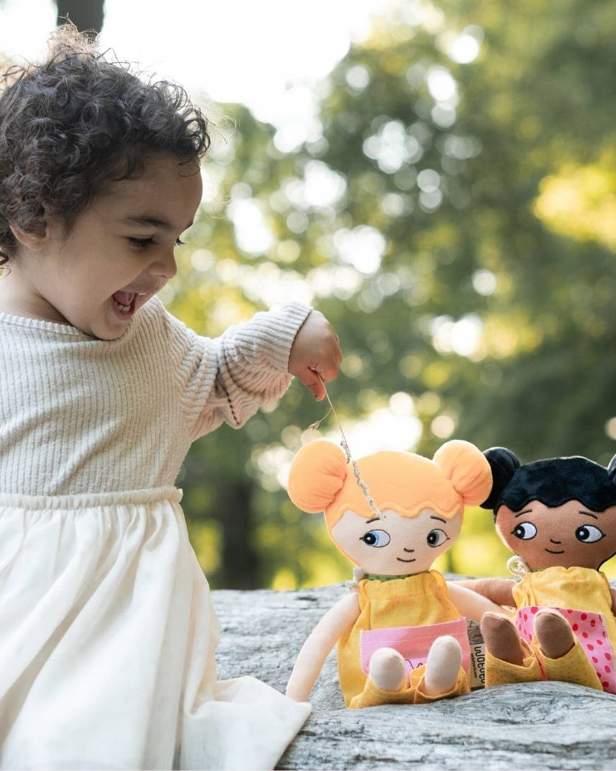 Flicka som leker glatt med sina watoto arts dockoar utomhus. Flickan matar sina dockor.