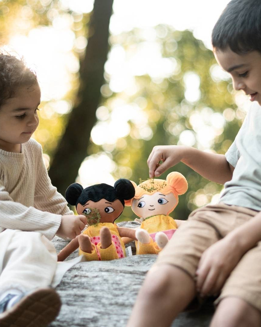 Två barn som sitter på ett träd och leker med sina watoto arts dockor. dockorna representerar barnens utseenden.