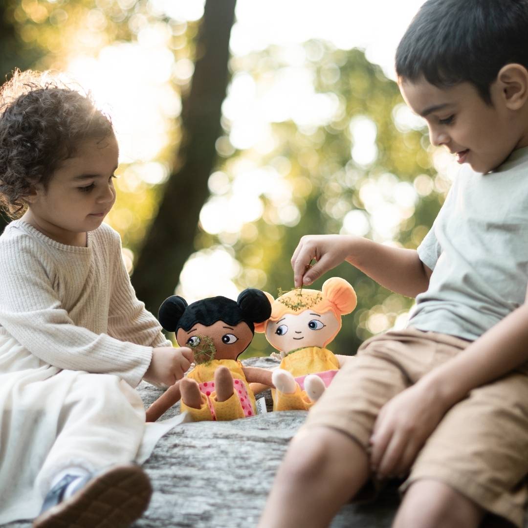 Två barn som sitter på ett träd och leker med sina watoto arts dockor. dockorna representerar barnens utseenden.
