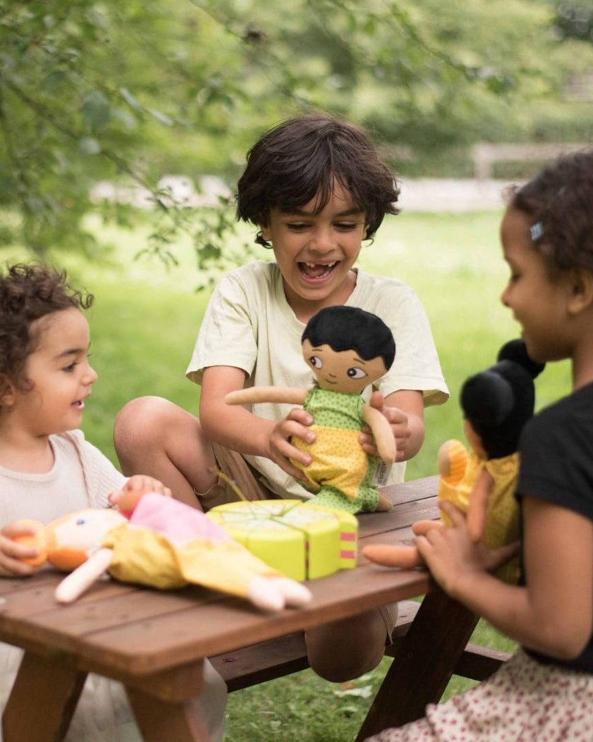 Tre barn som leker glatt med sina watoto arts dockor utomhus.