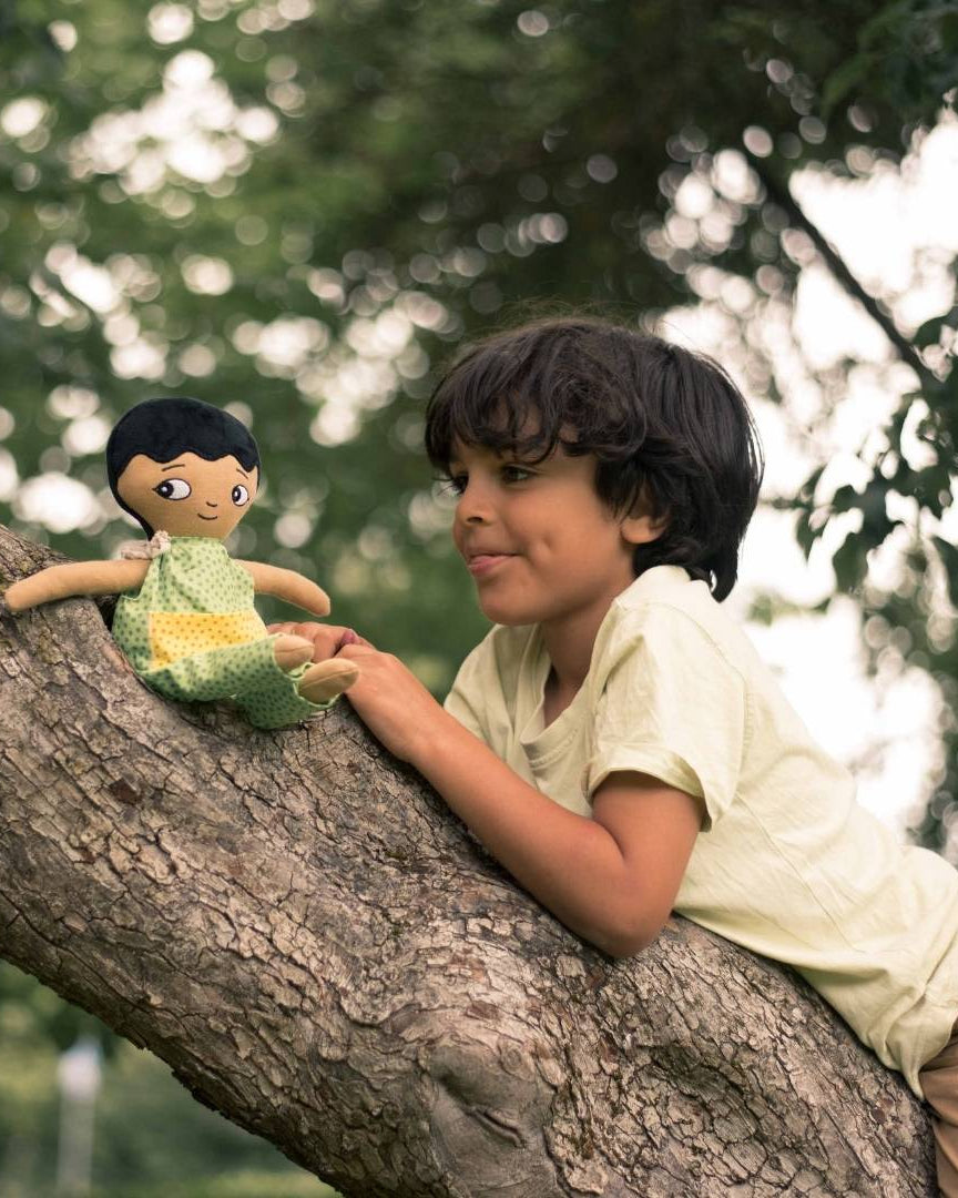 En pojke som är uppe i ett träd med sin watoto arts pojkdocka.