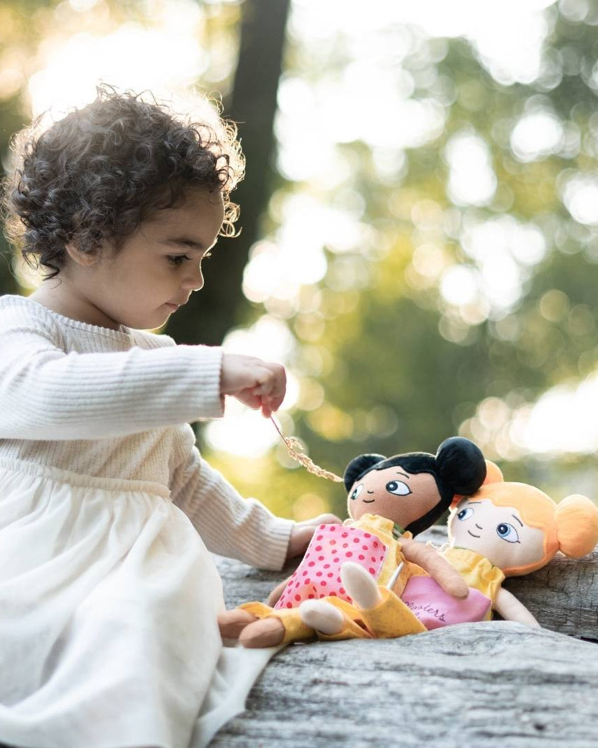 En flicka som leker med sina två watoto arts dockor utomhus. Hon matar sina dockor.