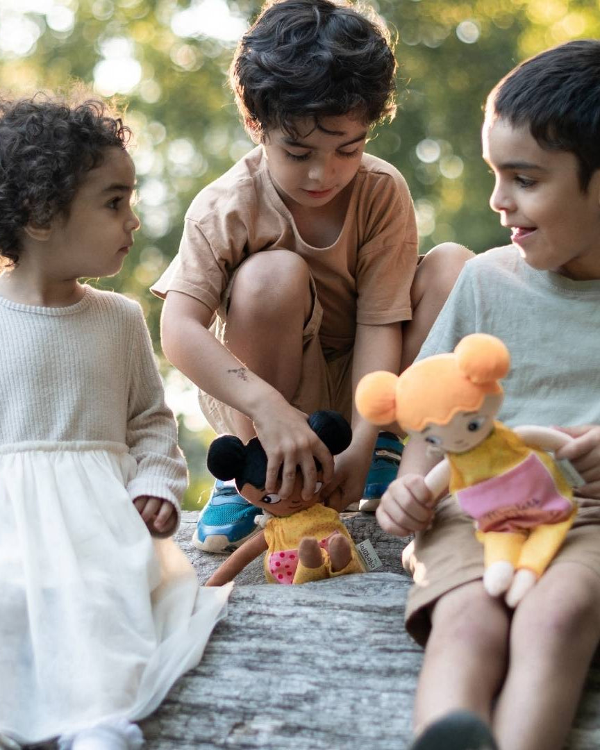 Tre barn som leker med sina watoto arts dockoar. dockorna har olika utseenden för att spegla många barn.