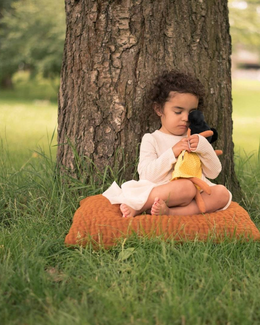 En flicka som kramar om sin watoto arts docka. Flickan sitter på gräset och lutar sig mot ett träd.