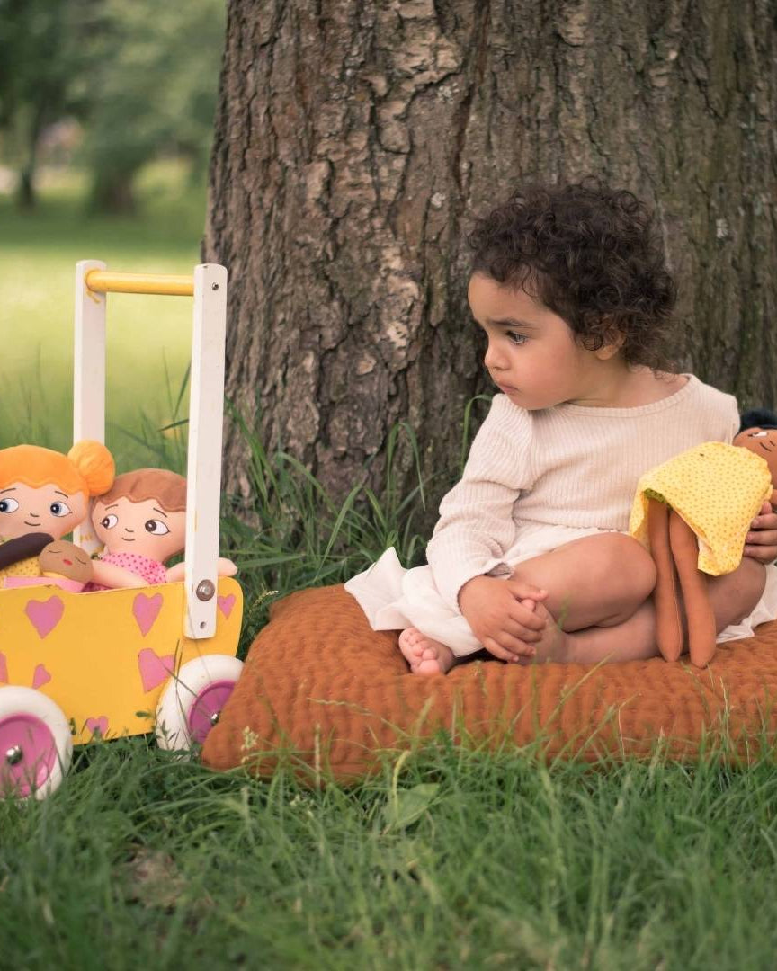 En flicka som kramar en watoto arts docka och har ytterligare tre dockor i en dockvagn. Bilden är tagen utomhus.