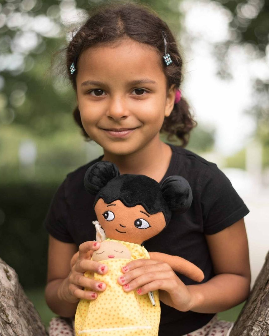 En flicka som sitter i ett träd och bär en watoto arts docka som representerar barnets utseende.