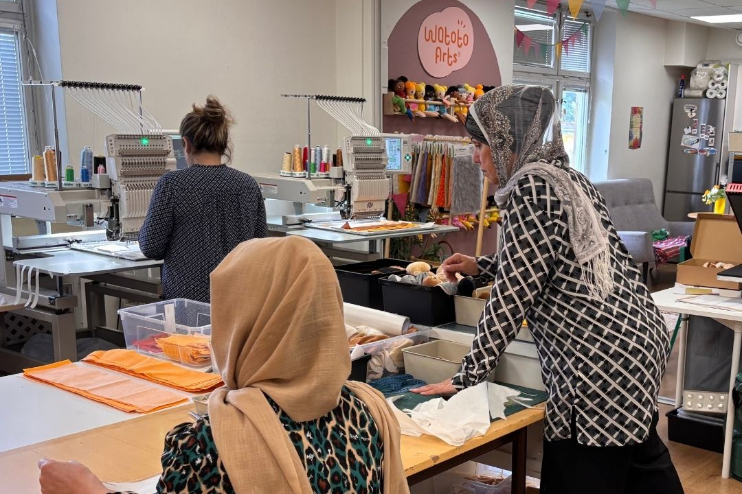 Three women with their backs turned, working on the production of dolls.