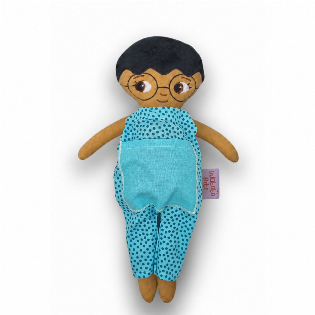 Mjuk tygdocka med kort svart hår, runda glasögon och blå prickig jumpsuit med blå ficka.