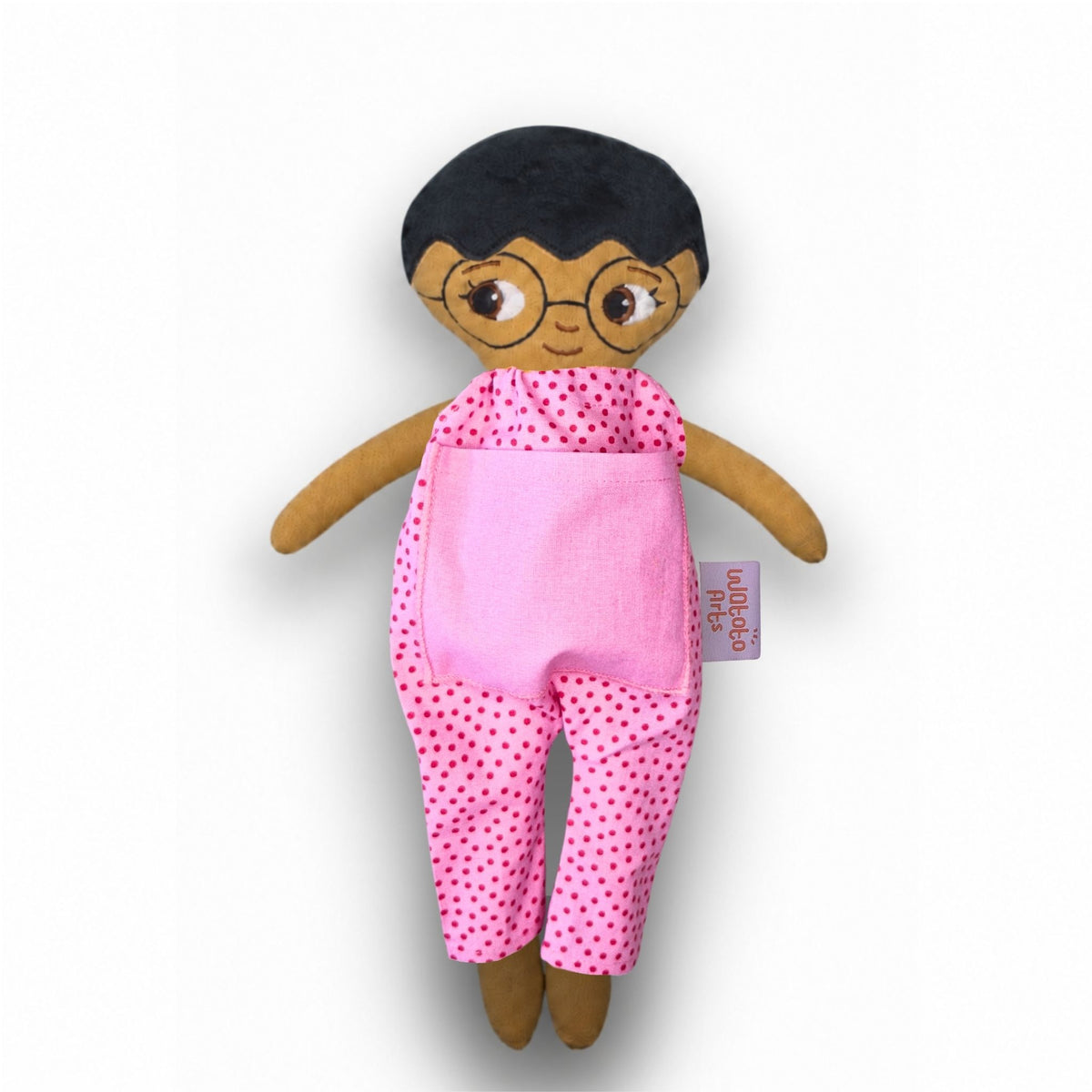 Mjuk tygdocka med kort svart hår, runda glasögon och rosa prickig jumpsuit med rosa ficka.