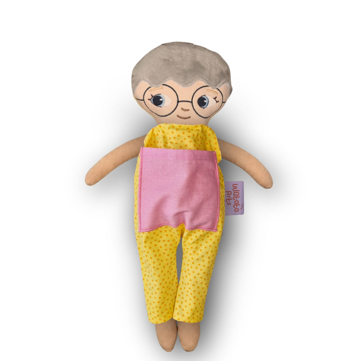 Docka med glasögon, vit hud, grått hår och blå ögon i gul jumpsuit med rosa ficka