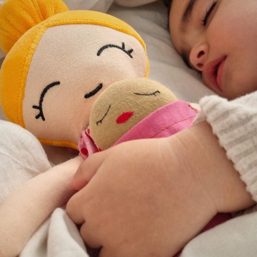 närbild på bebis som sover med dockan Maya med en bebisdocka i klädernas ficka