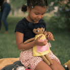 En flicka som leker med sin mjuka tygdocka utomhus på en picnick filt. dockan bär gul klänning.