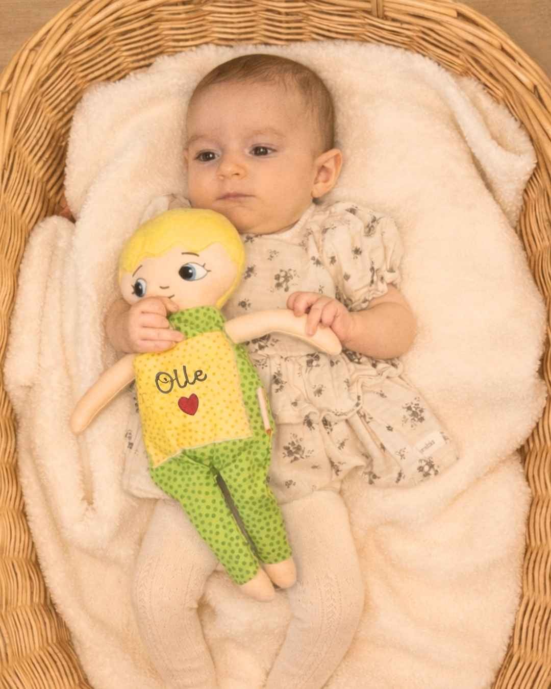 Dockan Adam som blir kramad av ett spädbarn som ligger i ett babynest