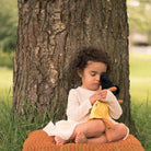 barn sitter vid ett träd och kramar sin mjuka docka i gul klänning