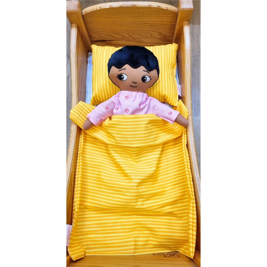 Pojkdocka från Watoto arts som bär pyjamas och liggen under det orangea täcket. 