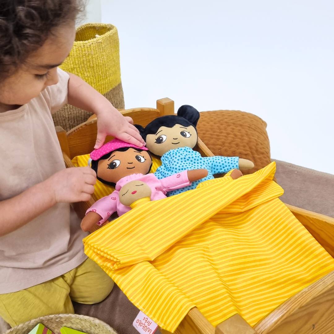 Flicka som leker med watoto arts dockor i en docksäng. Dockorna har på sig pyjamas och ska sova. 