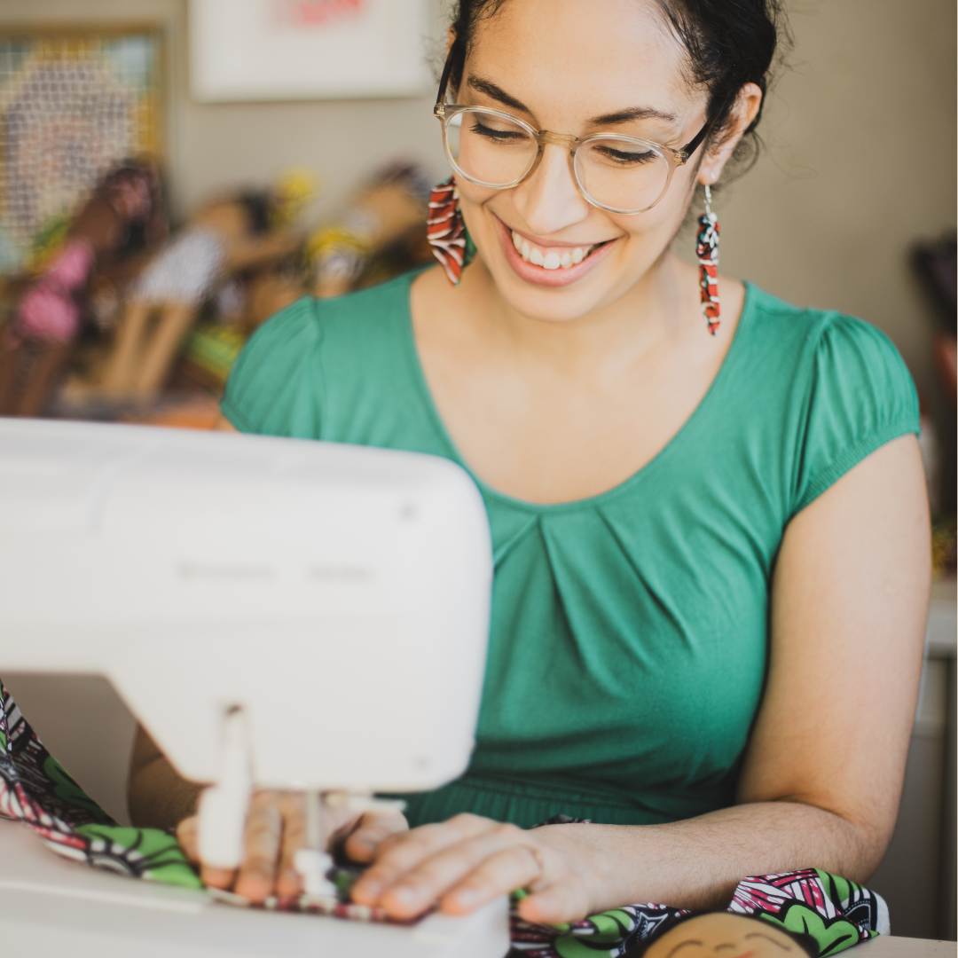 Fatma som sitter bakom en symaskin och syr en watoto arts docka för barn