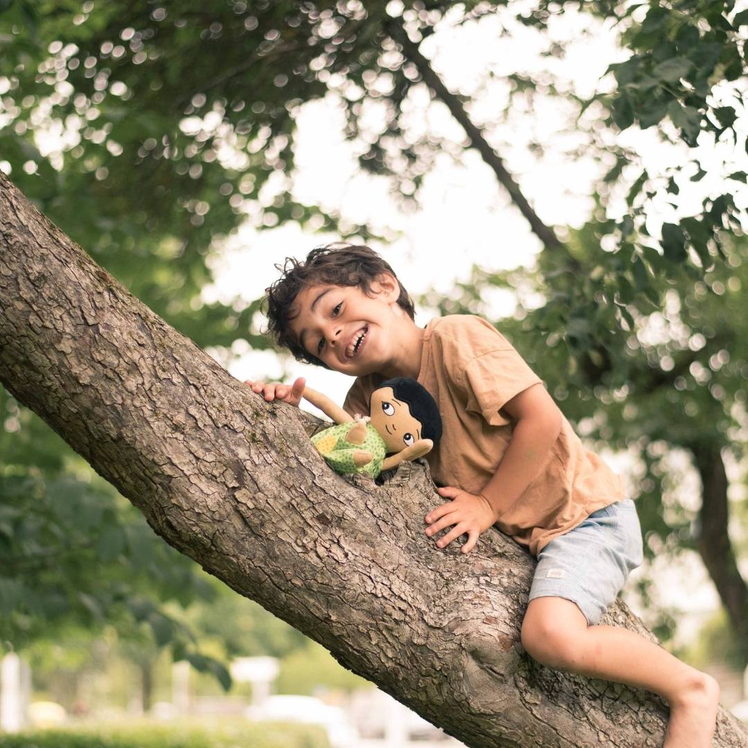 En pojke som klättrar upp i träd med sin watoto arts pojkdocka