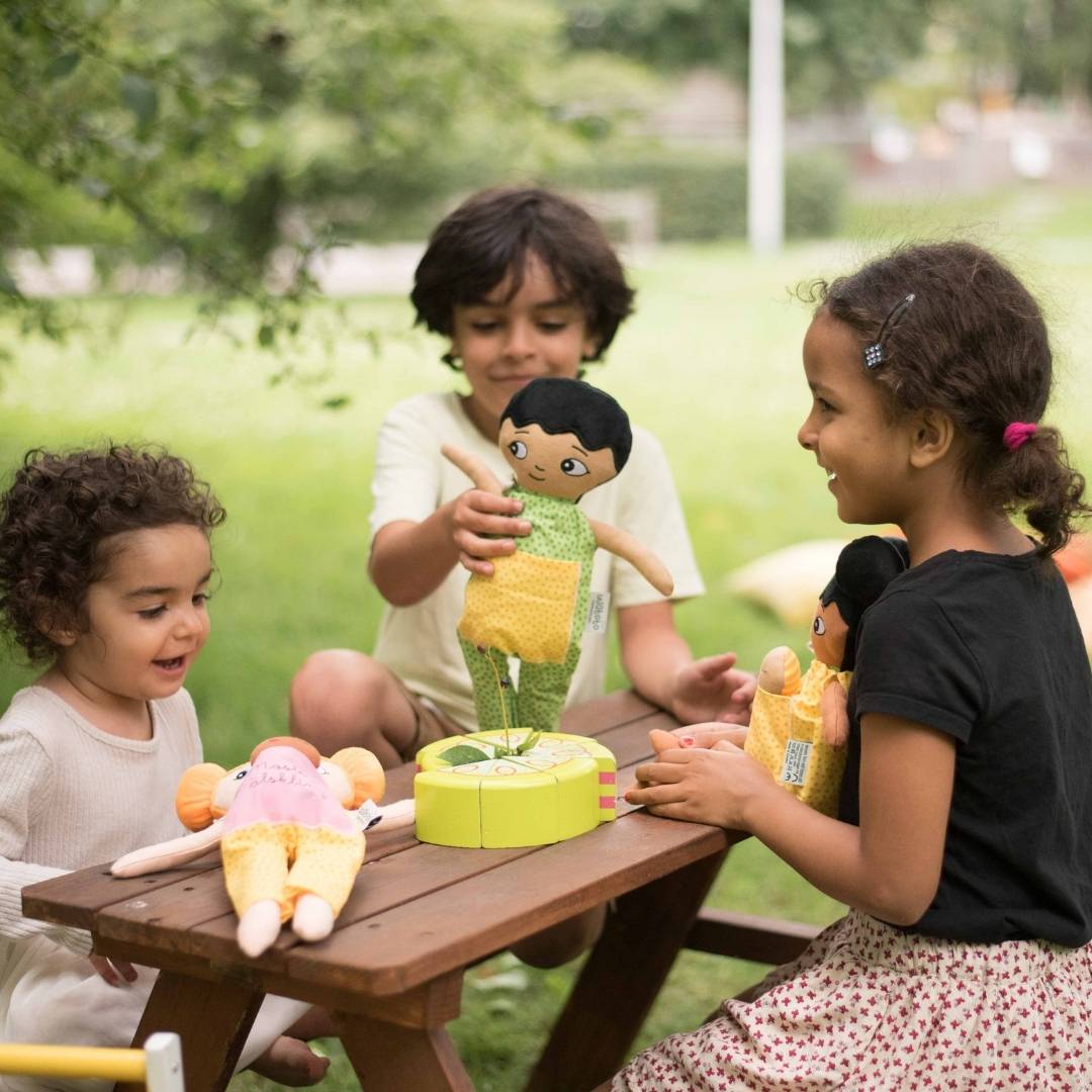 Tre barn barn som leker glatt med sina  Watoto Arts dockor utomhus. 