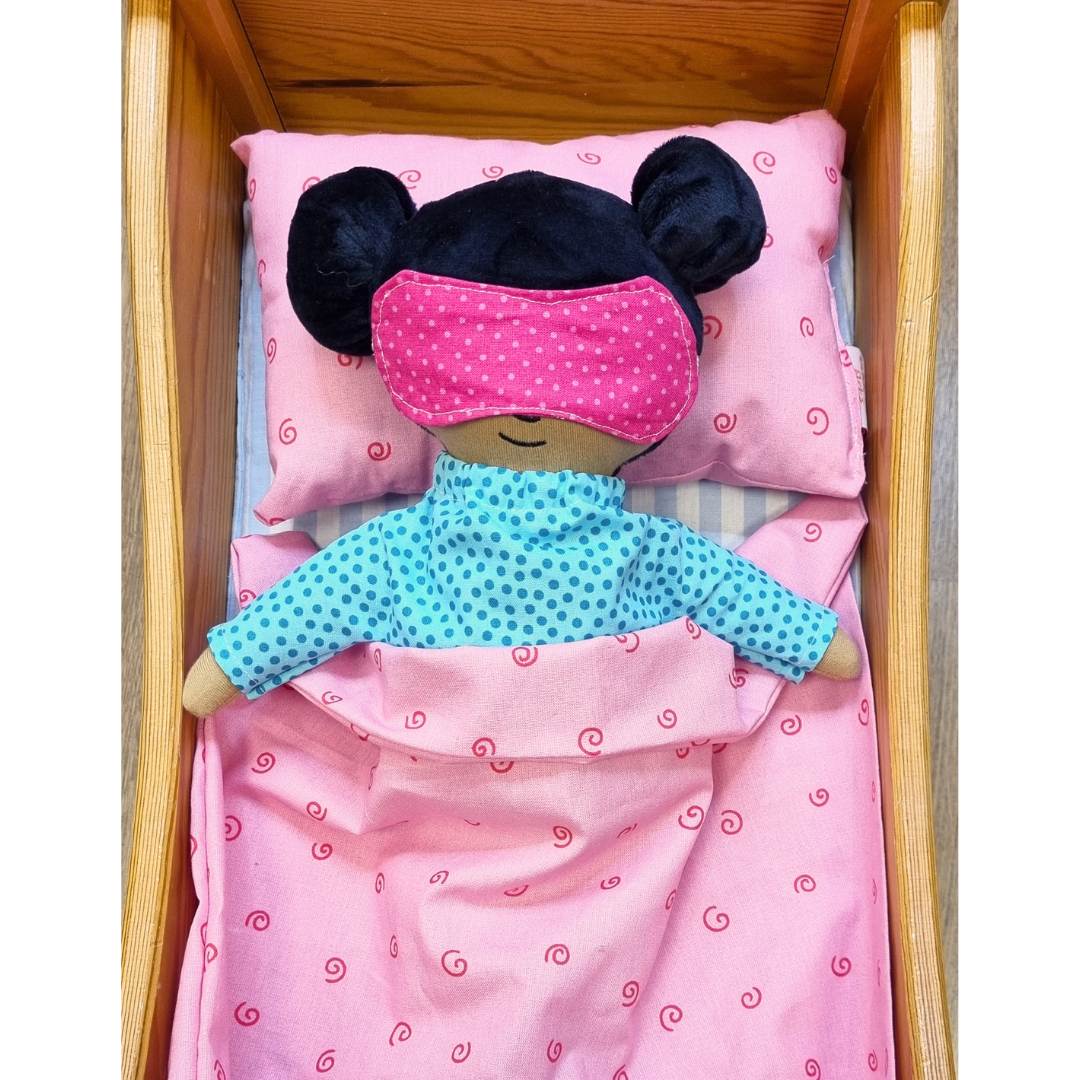 docka som sover i docksäng, dockan bär en sovmask och pyjamas
