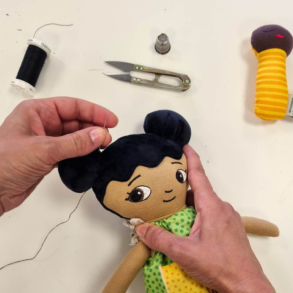 En watoto arts docka som tillverkas förhand. två händer som syr. 