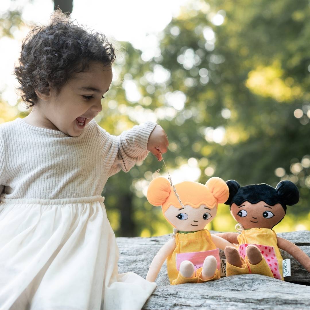 Flicka som leker glatt med sina watoto arts dockoar utomhus. Flickan matar sina dockor. 