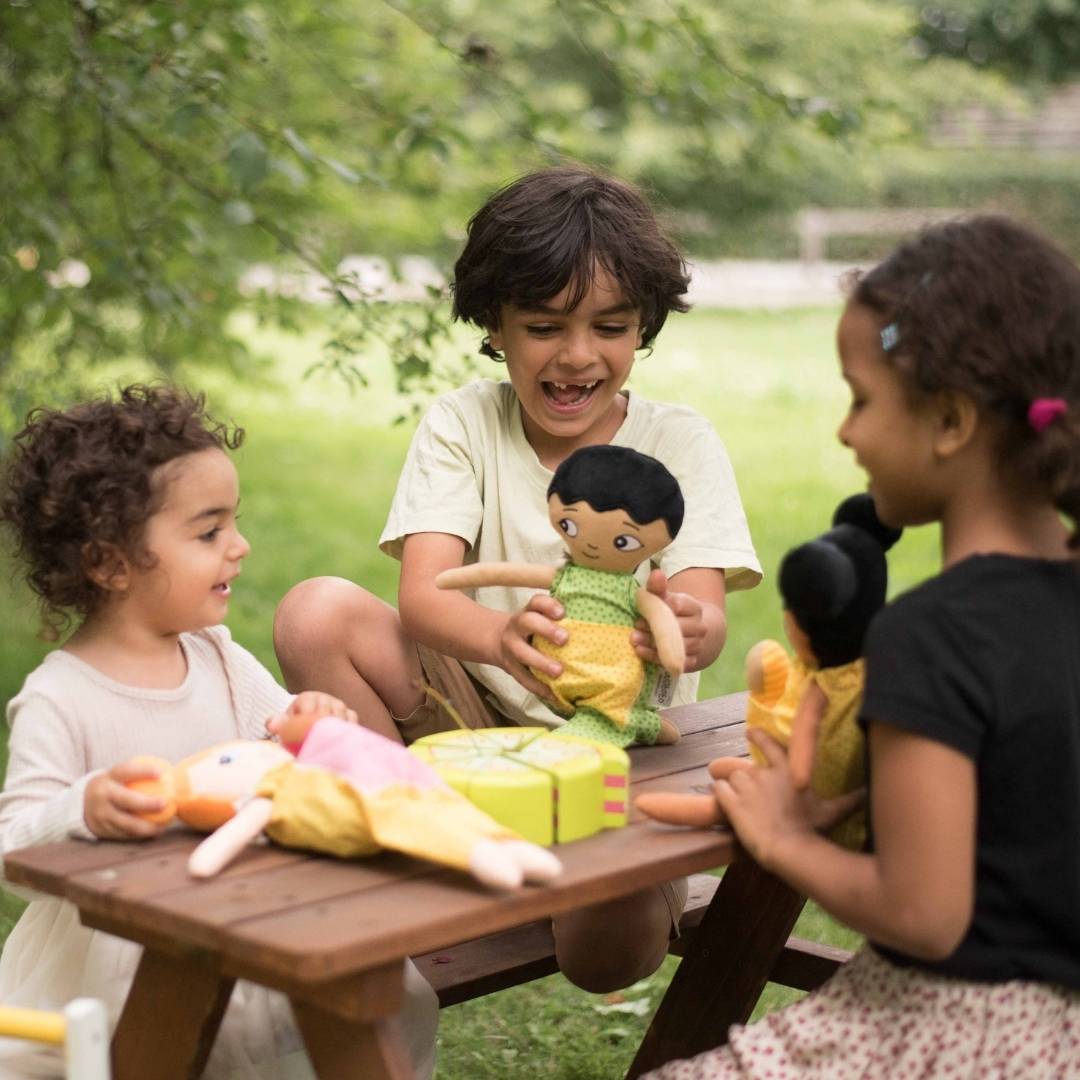 Tre barn som leker glatt med sina watoto arts dockor utomhus. 
