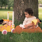 En liten flicka som sitter på gräset och leker med sina watoto arts dockor. hon har en dockvagn med dockor av olika hudfärger. 