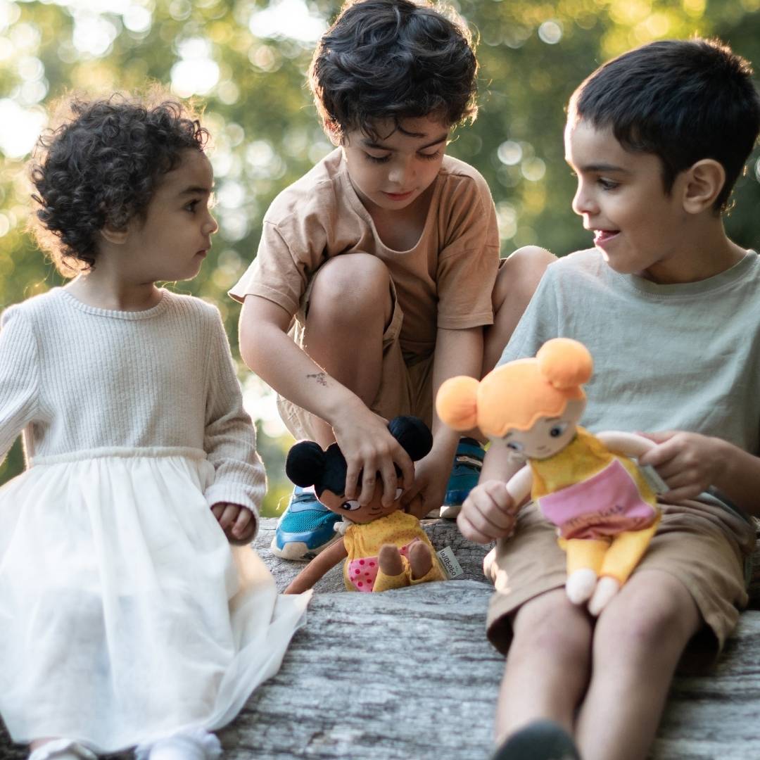 Tre barn som leker med sina watoto arts dockoar. dockorna har olika utseenden för att spegla många barn. 