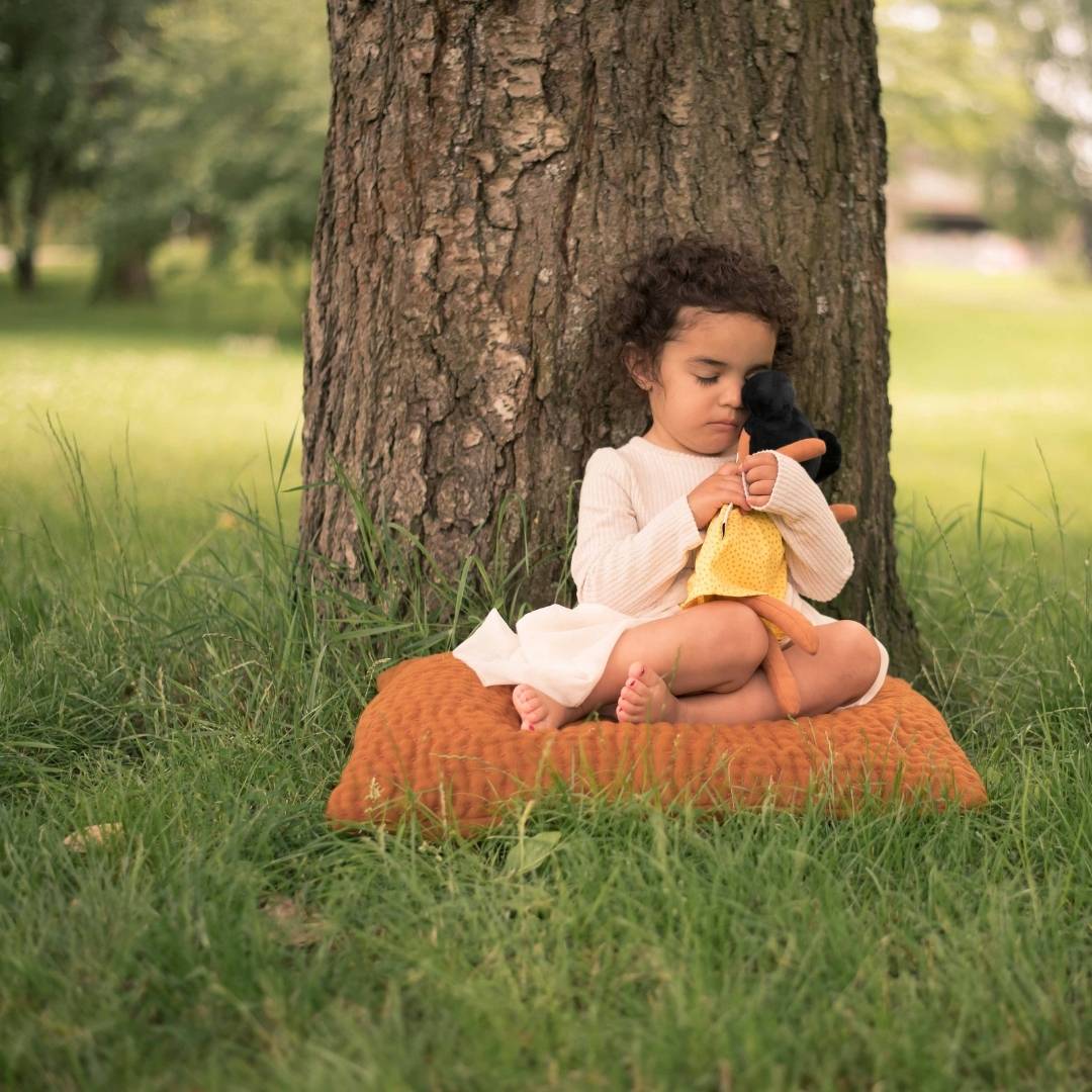 En flicka som kramar om sin watoto arts docka. Flickan sitter på gräset och lutar sig mot ett träd. 