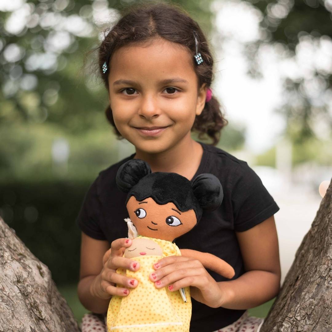 En flicka som sitter i ett träd och bär en watoto arts docka som representerar barnets utseende. 